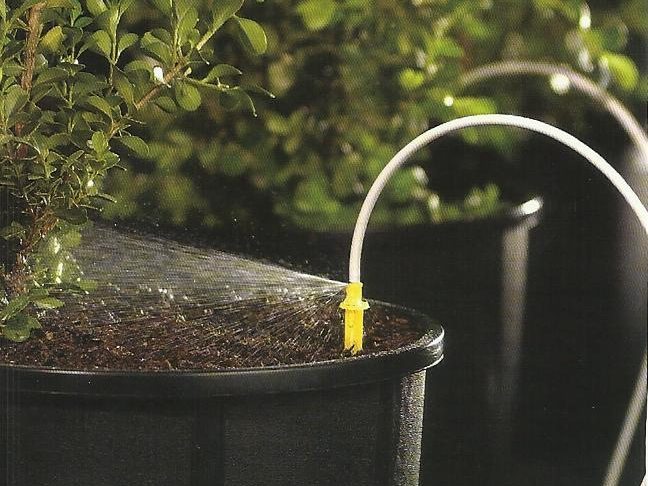 A spray stake on a feeder tube watering the surface of a container in a pot-in-pot nursery bed